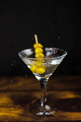 Martini glass with olive splash on dark background
