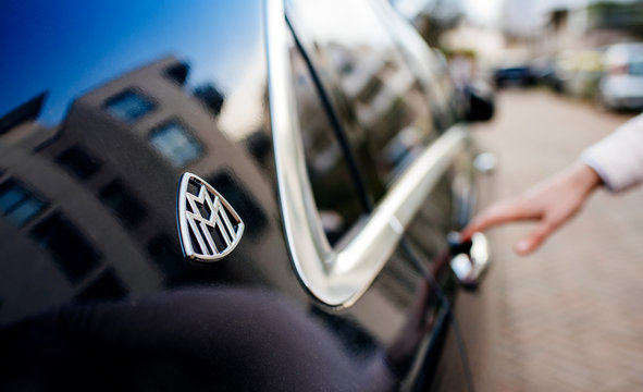 PARIS, FRANCE - APR 8, 2018: Silhouette of business woman entering the Luxury blue Mercedes-Maybach s600 limousine parked on a Parisian street near residential building - focus on the maybach logotype