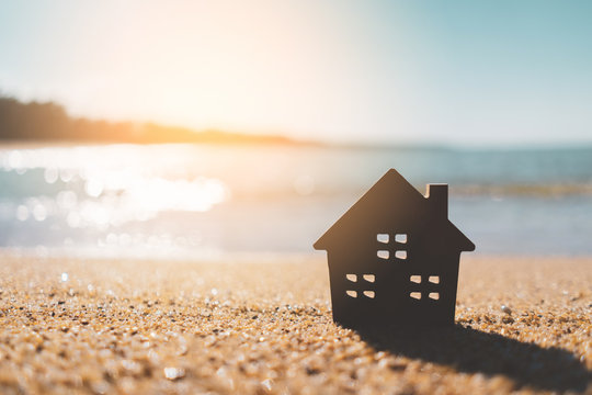 Small home model on sunset beach sand texture background.