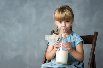 a little girl with pigtails in a blue dress drinking milk through a tube from a bottle