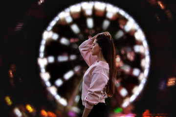 Young beautiful brunette woman happy in the city at night on the background of Park and Ferris wheel