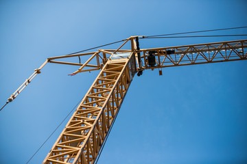 Naklejka premium Construction site with cranes on sky background. Big yellow machinery construction crane tool of building industry for heavy lifting on blue sky background. Business engineering equipment modern
