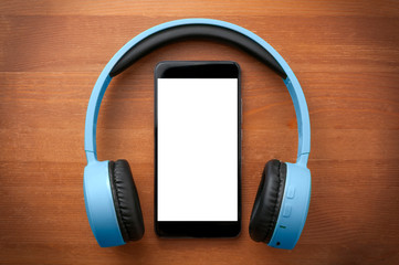 Pair of blue headphones around a blank screen smartphone on orange wooden table