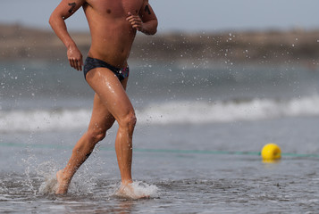 Swimmer running out of ocean finishing swim race.Fit man ending swimming sprinting determined out of water