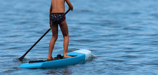 Child boy paddling on stand up paddleboard, paddle boarder