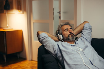 mid aged man listening music with headphones , relaxed in sofa at his home