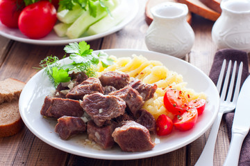 Beef stew with mashed potatoes on a white plate on a wooden table, horizontal