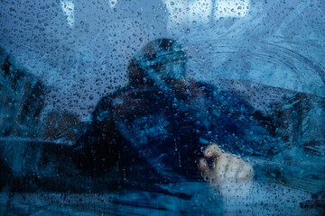 window dripping drops during the rain, a man stands behind the glass