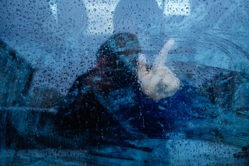 window dripping drops during the rain, a man stands behind the glass