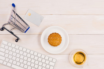 Online shopping concept. Computer keyboard, shopping cart, cake and tea with copy space.