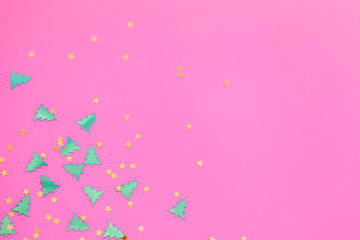 Fototapeta na wymiar Green metallic foil christmas trees and gold stars confetti sparse on pink background. Simple holiday concept. Design template. Frame with copy space. Winter festive backdrop. Top view, flat lay.