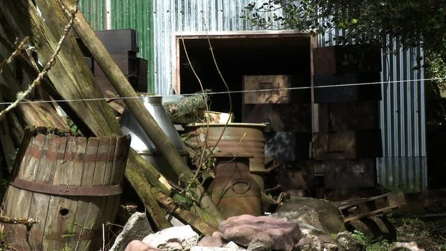 Wide shot of fenceposts, broken barrels, and rocks piled up by a tin shed