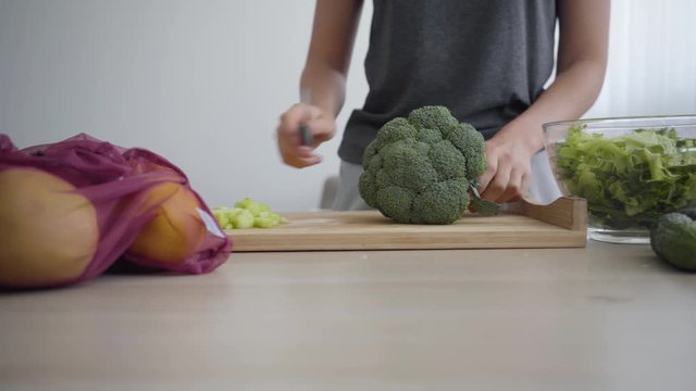 Female hands putting lettuce in deep bowl then taking broccoli and start cutting. Unrecognizable woman cooking breakfast in the kitchen. Healthy lifestyle. Profession of nutraceutical, nutritionist