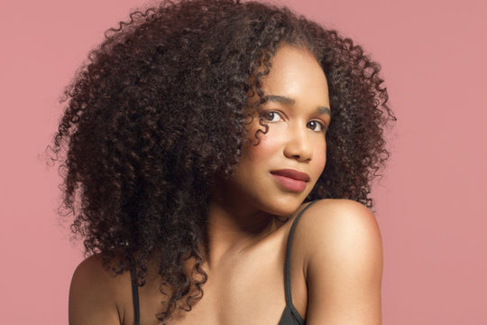 closeup portrait of young mixed race model with curly hair in studio with natural neutral makeup with big afro hair on pink