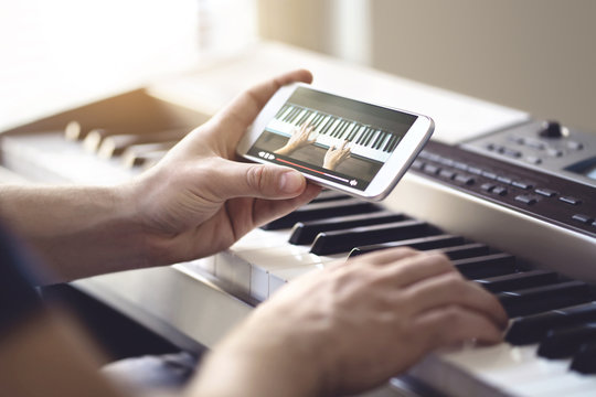 Piano Lesson Online. Man Watching Video Tutorial With Mobile Phone And Practising Playing. Person Learning To Play An Instrument With An Internet Course And Class. Pianist Training With Smartphone.