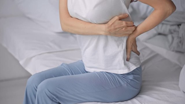 cropped view of woman sitting on bed with backache