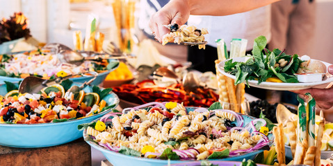 Close up view of people firends hands taking food from catering table during party celebration - food on a table -coloured background and together