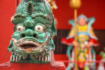 Close-up of traditional Chinese art statue animal head with a blurry background of Chinese temple. Green dragon head on vivid red and yellow temple background.
