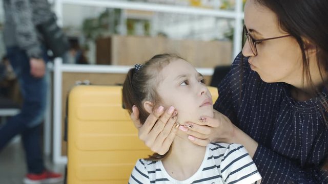 Mom combs her hair a little cranky daughter in the airport lobby, close-up.