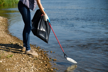 Volunteer woman picking up plastic garbage on coast of the river. Cleaning environment concept