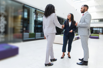 Diverse business partners greeting each other in hallway. Business man and women standing in office...