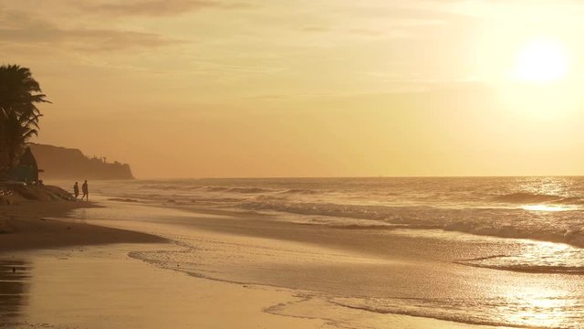 People in the sunset at a tropical beach with palm trees and the pacific ocean. South America, Peru