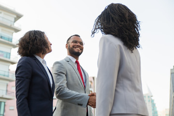 Positive business partners meeting outside. Business man and women standing shaking hands, talking and smiling. Communication concept