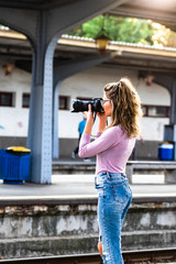 Young girl walking alone on train platform and taking photos on railway station