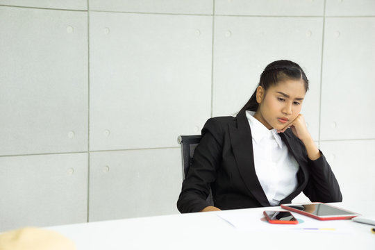 Thoughtful Young Businesswoman With Hand On Chin Sitting At Desk Looking At Mobile Phone. Well-dressed Asian Female Executive With Introspective Manner.