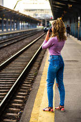 Young girl walking alone on train platform and taking photos on railway station