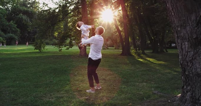 At sunset dad with his small boy playing in the park taking his son in hands and enjoying the time , they wearing stylish clothes