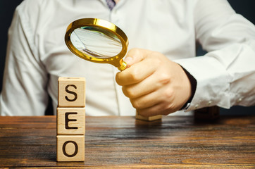 Blocks with the word SEO and a magnifying glass in the hand of a businessman. Search Engine...
