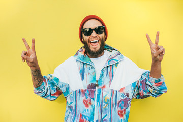 Stylish young hipster man with beard in red hat and a retro jacket of 90s on yellow...
