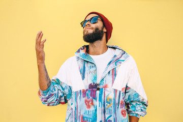 Stylish young hipster man with beard in red hat and a retro jacket of 90s on yellow...