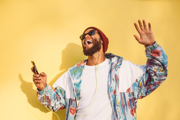 Stylish young hipster man with beard in red hat and a retro jacket of 90s on yellow background...