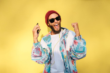 Stylish young hipster man with beard in red hat and a retro jacket of 90s on yellow background...