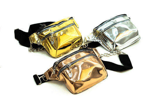 Gold, orange and silver glossy travel belt bags with metal chain strap and zipper for women placed looking upside on an isolated white background - side view.