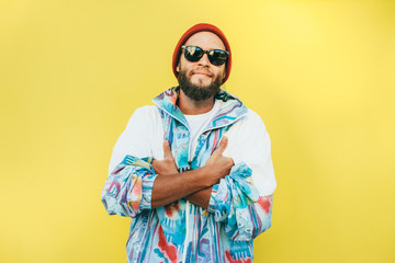 Stylish young hipster man with beard in red hat and a retro jacket of 90s on yellow...