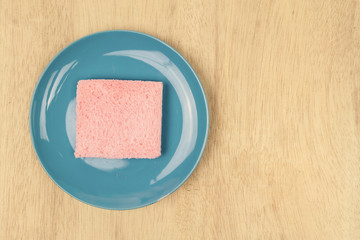 Top view of pink milk flavored sandwich bread on blue sky ceramic plate and wooden background, warm tone.