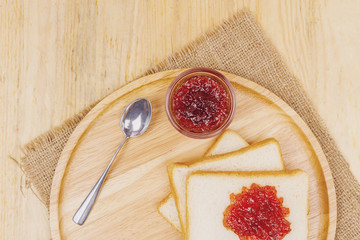 Top view of sliced bread and strawberry jam on wooden background closeup, soft warming tone.