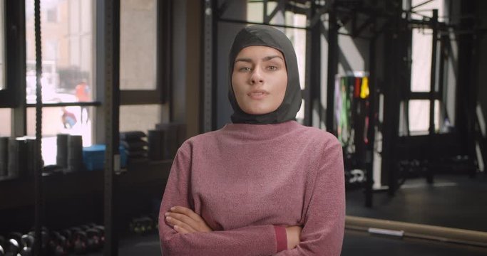 Closeup portrait of young attractive athletic muslim female looking at camera with her arms crossed over chest in gym indoors