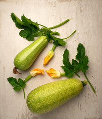 Fresh ripe green zucchini fruits with leaves and flowers on a white table .