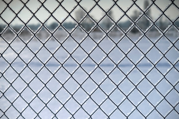 Fence with mesh netting covered with frost with blurred background