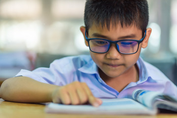 Asian elementary school boy in a white school uniform and wearing glasses, is doing homework in the classroom.