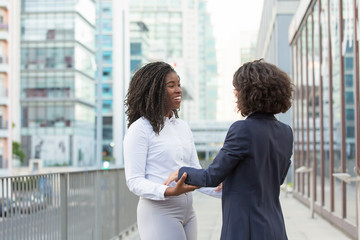 Happy old female friends accidently meeting in business district. Business women standing in city street and hugging. Surprise or meeting concept