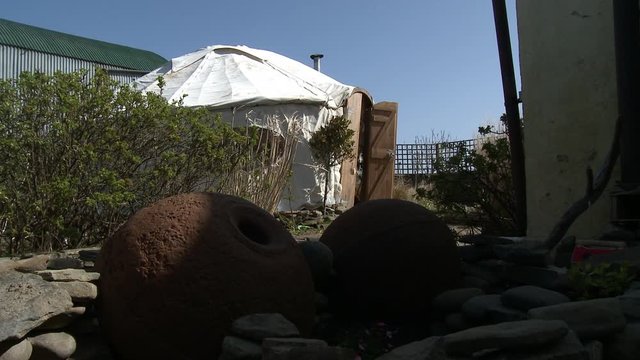 Flowers pots and rocks in the foreground in the shade, with a white canvas tent in the background