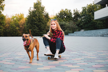 Teenage skater girl having fun with her dog in the city. Mixed breed dog pulls young woman riding a skateboard in urban park © Photoboyko