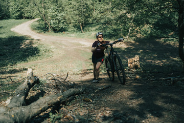 Photo of sportswoman in helmet raising bicycle to hill in forest