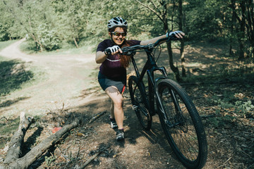 Fototapeta na wymiar Photo of sportswoman in helmet raising bicycle to hill in forest