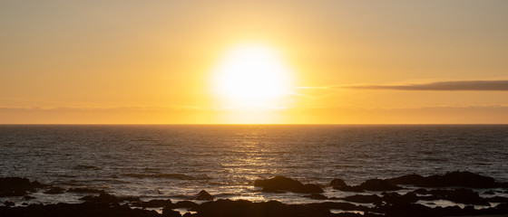 Sun shining brightly on horizon at sunset over ocean with golden reflections on the waves